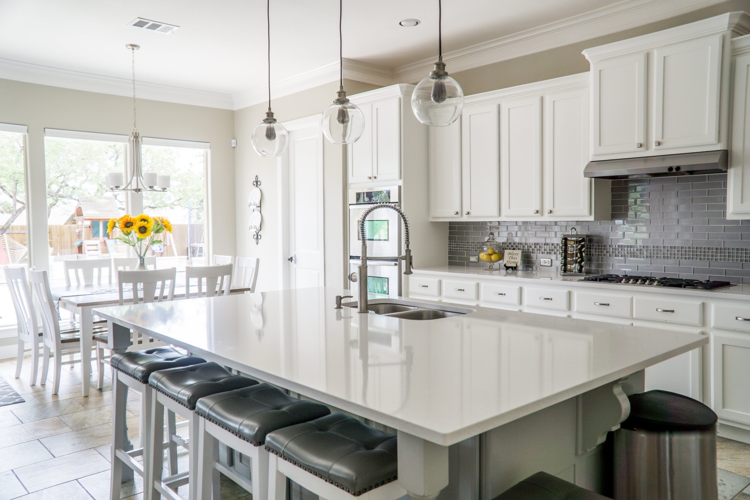 A white kitchen with a center island and stools, featuring glass splashbacks that require regular cleaning.