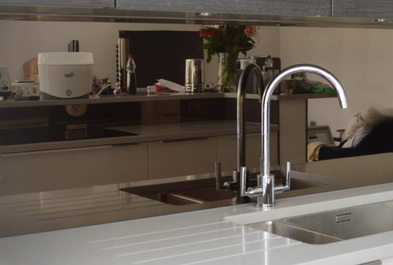 Modern kitchen interior with reflective countertops, a sink, faucet, and various appliances in a gray color scheme.
