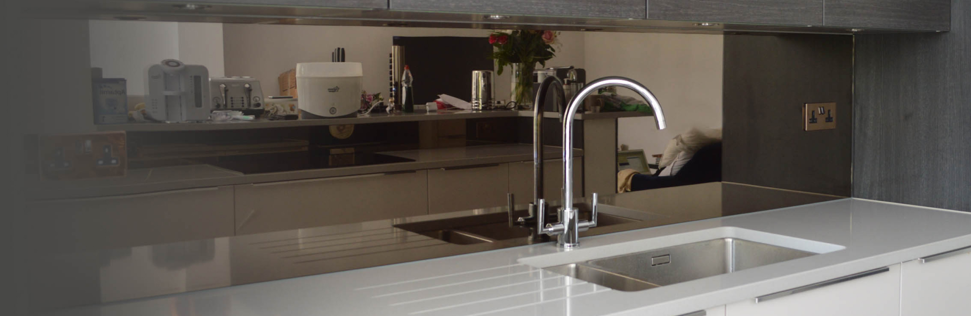 Modern kitchen interior with reflective countertops, a sink, faucet, and various appliances in a gray color scheme.