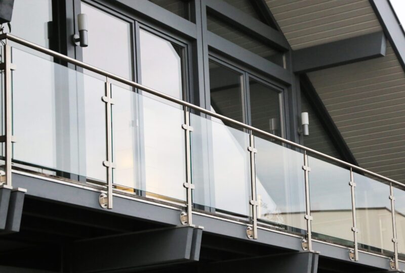 Modern building facade featuring large glass windows and a metal balcony railing, with new architectural details in grey tones.