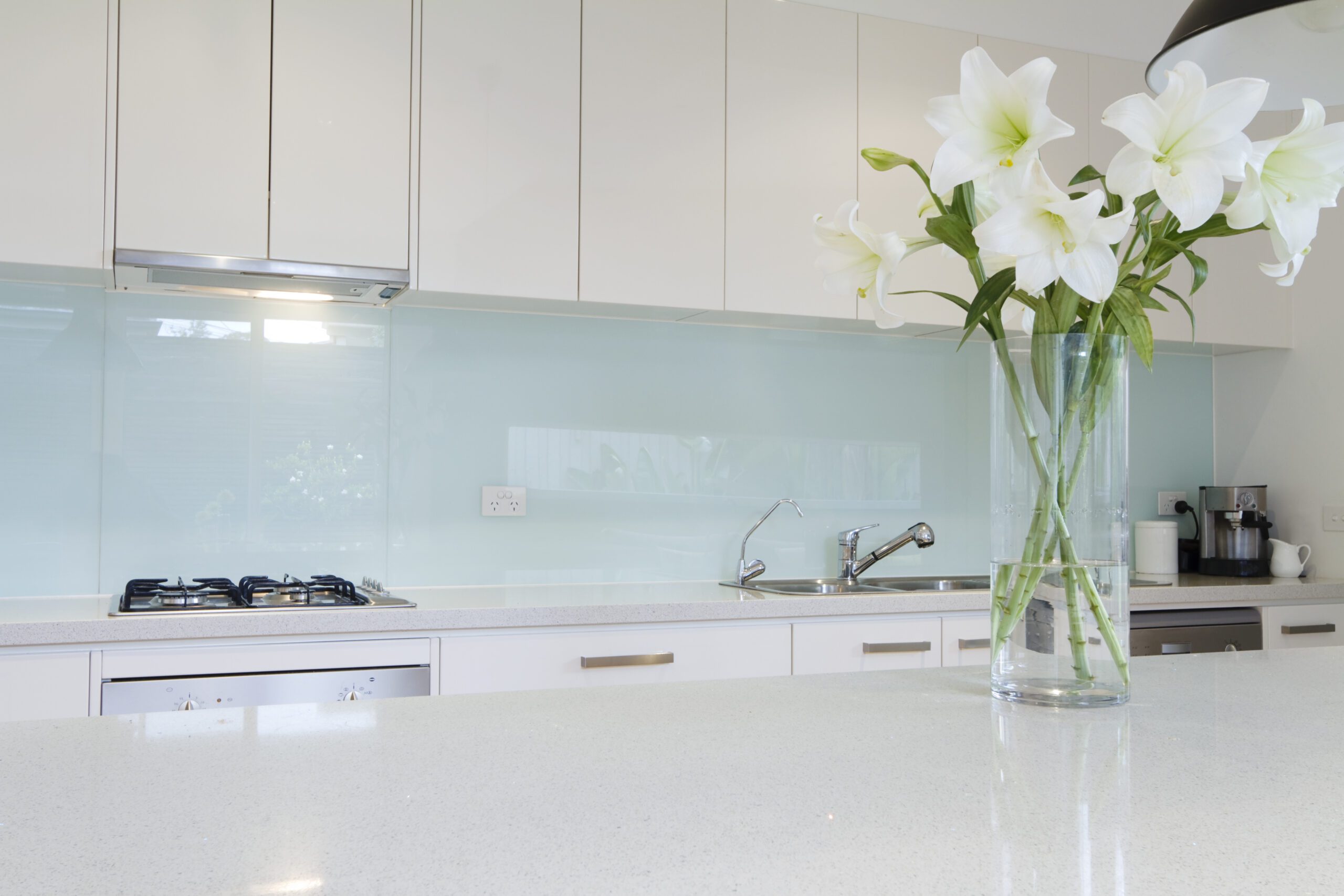 Modern kitchen interior with white cabinets, a gas stove, and a glass vase of white lilies on the countertop.